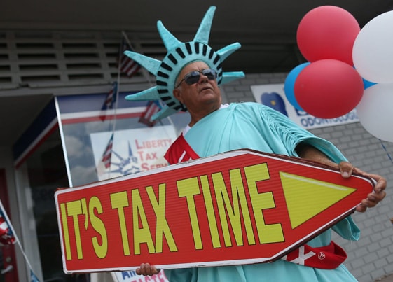 Man wearing a statue of liberty costume holding a sign that says "It's tax time."
